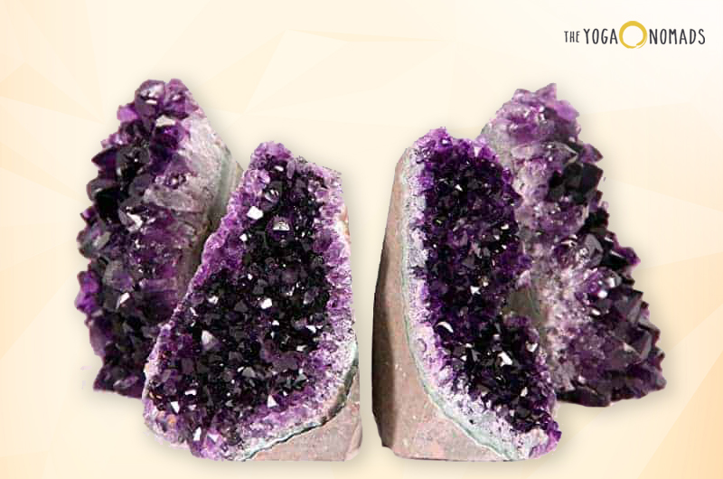 A pair of amethyst geodes with a deep purple crystalline structure inside and a rough, lighter-colored exterior. The crystals are arranged in a typical geode pattern, with pointed formations facing inward towards the hollow center of each half. The background is pale yellow with a gradient effect.