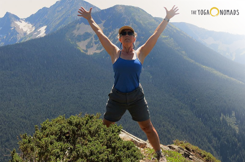 The image shows an individual standing on a rock with arms raised against a backdrop of mountains and clear skies.