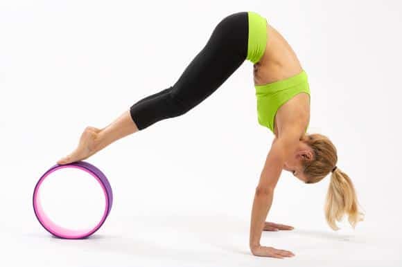 An individual performing a yoga pose with the aid of a yoga wheel. The person is in an inverted position, supporting their body with their hands on the ground and feet elevated on the yoga wheel.