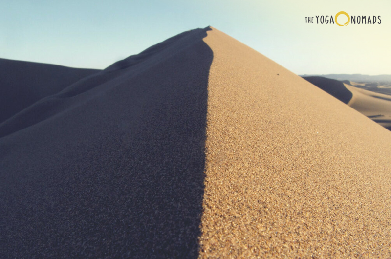 Is yin good or bad? The image captures a close-up view of a sand dune, highlighting the sharp contrast between the shadowed and sunlit areas of the sand. The sky is visible in the background, indicating it is daytime.