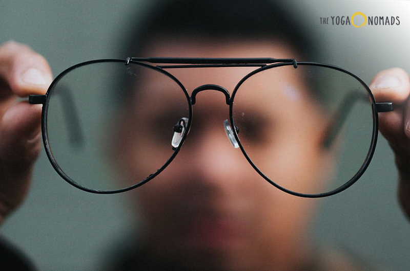 person holding his glasses in a closeup portrait shot that blurs the background.