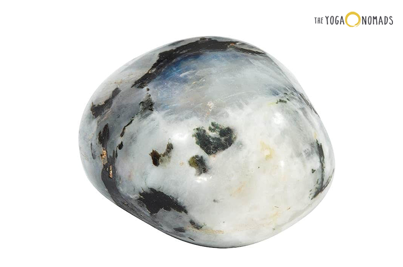 A polished stone with a predominantly white color and patches of black and dark blue. The stone has an oval shape and displays an iridescent sheen, characteristic of rainbow moonstones.